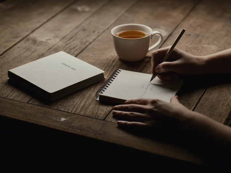Illustration de mains qui écrivent dans un cahier à spirale, à côté d'une tasse de thé